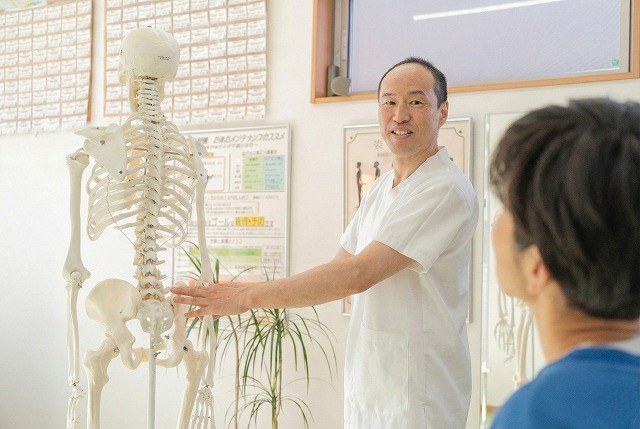 骨格模型を使って痛みの原因と改善方法を笑顔で説明する整体師